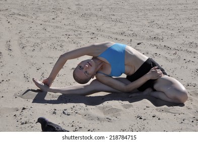 Bald Woman Exercising Yoga Side Bend, Or Parivritta Janu Sirsasana, On A Sandy Beach.