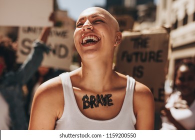 Bald woman laughing outdoors during a protest. Brave woman with group of protesters in background.
