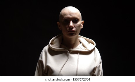 a bald woman looks sadly into the camera, light passes through her face from light to dark. on a black background