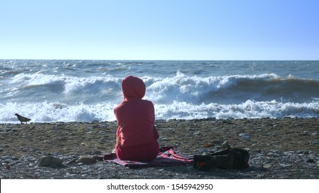 Bald Woman In A Sweatshirt Sits On The Seashore During A Storm.