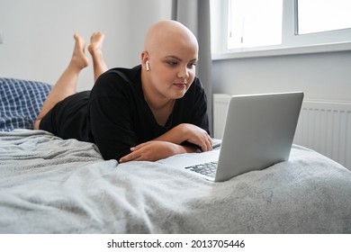 Bald Woman Wearing Earphones Working At The Laptop While Laying On The Bed