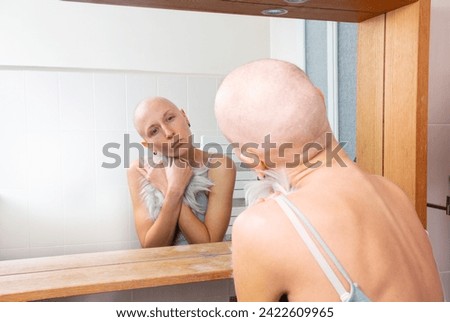 Bald young woman is caught in a moment of introspection while holding a substitute strand of hair in a mirror's reflection