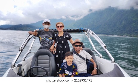 Bali, Indonesia, 05, May, 2022, A Family, With Two Sons, One Of Whom Wears A White Hat, And A Father, And Mother, Posing On A Spitbot, In The Middle Of A Lake At A Tourist Spot In Bali