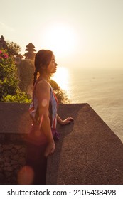 Bali - Indonesia - 10.21.2015: Asian young female with braided dark hair watching the sea at sunset - golden hour at Uluwatu Temple - sun flare
