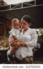 BALI, INDONESIA - Feb 03, 2022: Indonesian Woman In Traditional Clothes With A Baby Child, Indonesian Family During Hindu Religious Ceremony In Bali