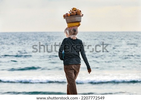 Bali, Indonesia - February 19 2017: Rear view of a woman carrying on her head a basket full of fruit