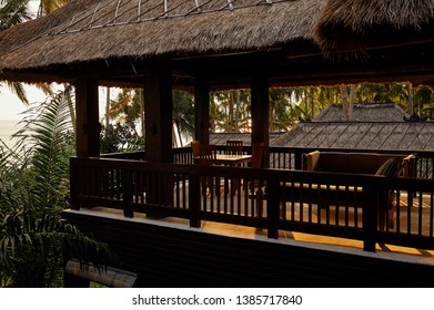 Bali, Indonesia, January 2016. Second floor of the old wooden house with 
thatch roof in a warm sunset light, with tropical trees on the background