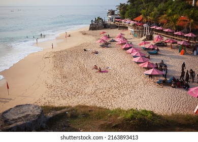 Bali, Indonesia - May, 29, 2022: Dreamland beach with pink umbrellas and sunnbeds on white sand at sunset. Background with copy space for design.