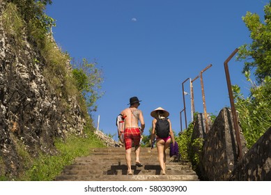 BALI, INDONESIA - Oct 6, 2016: Young Sporty Young Caucasian Couple With Hat And Surf Board Walking Up The Stairs. Blue Sky With Big Moon.