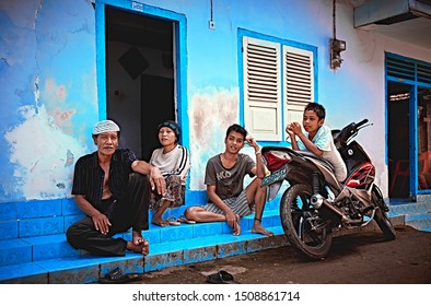 Bali, Indonesia - Sep 19, 2019: Family Portrait Of A Rural Indonesian People Sitting On The Street In Front Of Their Traditional House.