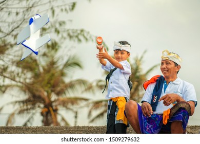 Bali / Indonesia - Sept 14th 2019 . Balinese Kid And His Fatherdressed In Traditional Custom Playing With Airplane Polystyrene Toy During A Pause At Hindu Sacred Ceremony 