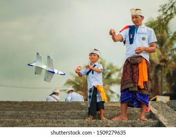 Bali / Indonesia - Sept 14th 2019 . Balinese Kid And His Fatherdressed In Traditional Custom Playing With Airplane Polystyrene Toy During A Pause At Hindu Sacred Ceremony 