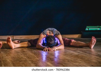 Bali, Indonesia - September 2017: Flexible Man In A Seated Forward Fold (Dragonfly Pose) Wearing Neon Headphones During A Silent Disco Event