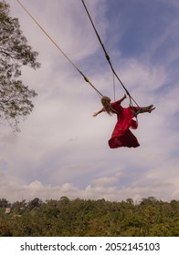 Bali Swing Trend. Caucasian Woman In Long Red Dress Swinging In The Jungle Rainforest. Vacation In Asia. Travel Lifestyle. Blue Sky With White Clouds. Bongkasa, Bali, Indonesia