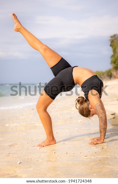 Bali yoga. Young\
woman practicing Eka Pada Chakrasana, One Legged Wheel Pose. Upward\
facing bow pose is a deep backbend. Straight leg. Yoga retreat.\
Thomas beach, Bali,\
Indonesia