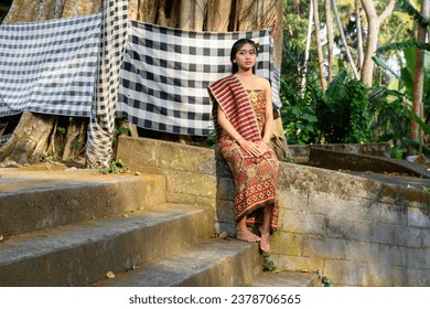 Balinese girl in festive clothing and headdresses sit on the steps of a temple - Powered by Shutterstock