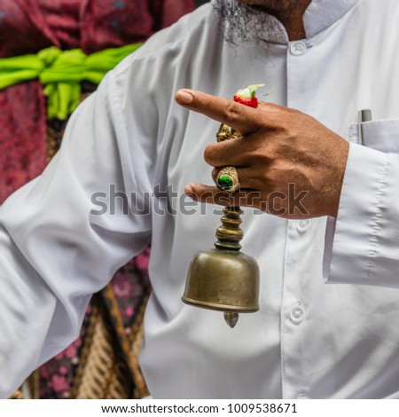 Balinese Hindu priest pemangku dressed in white holding a bell (Bidschel) during family tiga bulanan ceremony. Bali, Indonesia. Square image