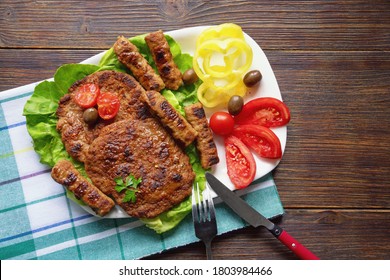 Balkan cuisine. Pljeskavica and cevapi - grilled dish of minced meat - with vegetables. Flat lay, copy space