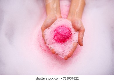 A ball of bath salt dissolves in water in female hands.