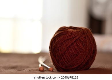 A ball of brown woolen threads and two wooden knitting needles close-up. Preparation for knitting. 