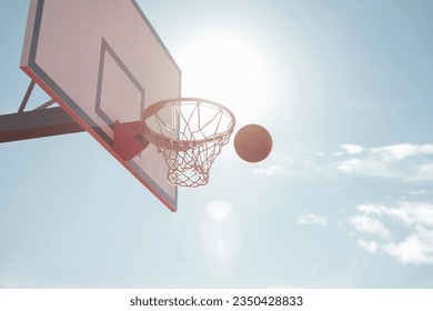 The ball flies into the basketball hoop against the background of the sky and the setting sun. Big White Basketball Shield - Powered by Shutterstock