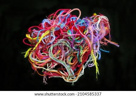 Ball of multicolored tangled cotton threads and yarn for needlework close-up on black background