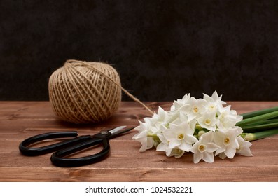 Ball of twine with retro flower scissors and white narcissi blooms on a wooden table