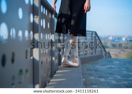 Ballerina in ballet legs in shoes and black tutu dancing by the fence. Beautiful young woman in black dress and pointe dancing outside. Gorgeous ballerina performing a dance outdoors. Close up