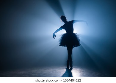 Балерина в черном платье-пачке танцует на сцене с волшебным синим светом и дымом. Силуэт молодой привлекательной танцовщицы в балетных туфлях, выступающих в темноте. Пространство для копирования.