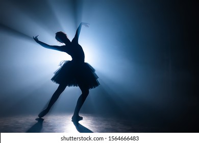 Ballerina In Black Tutu Dress Dancing On Stage With Magic Blue Light And Smoke. Silhouette Of Young Attractive Dancer In Ballet Shoes Pointe Performing In Dark. Copy Space.