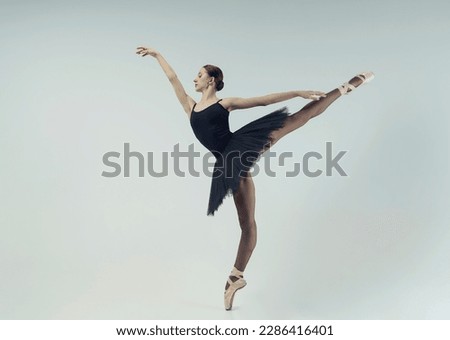 a ballerina in a black tutu shows an arabesque in a photo studio