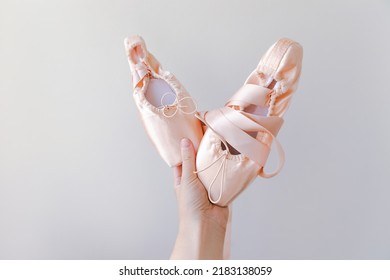 Ballerina dancer hand holding new pastel beige ballet shoes with satin ribbon isolated on white background. Ballerina classical pointe shoes for dance training. Ballet school concept. Copy space