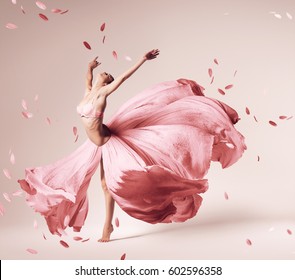 ballerina dancing in flowing pink dress with flying petals in studio