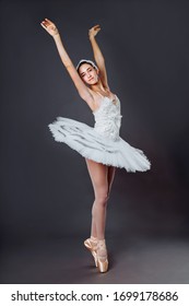 Ballerina Dancing In White Dress. Color Photo. Graceful Ballet Dancer Or Classic Ballerina Dancing Isolated On Grey Studio Background. Ballerina On Point Shoes Feet Tutu From Lake Swan