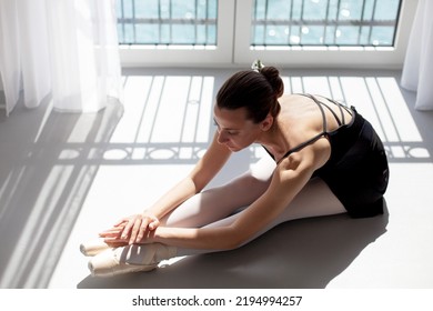 Ballerina In Pointe Shoes At Home. Dancer Sitting On Floor By Big Window Above Sea In Sunlight. Girl Doing Exercises And Stretching. Dance Workout In Ballet Class Room. Woman In Body Ballet Studio