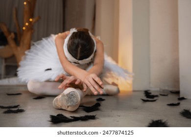 Ballerina portrays dying swan in the Swan Lake Ballet. Ballet dancer in pointe shoes lies on the floor among black fallen feathers. Talented theater actress. Shadow light interior. Faceless girl - Powered by Shutterstock