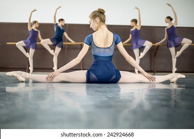 ballerina sitting on the floor with his back to the camera in the splits and dance class dancers practicing on the background - Powered by Shutterstock