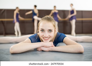 ballerina sitting on the floor with his face to the camera in the splits and dance class dancers practicing on the background - Powered by Shutterstock