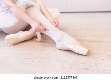 A Ballerina Sitting On The Floor Tying Her Ballet Shoes