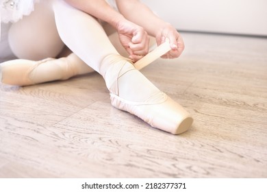 A Ballerina Sitting On The Floor Tying Her Ballet Shoes