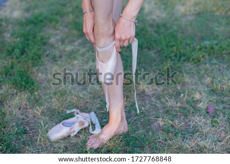 Ballerina standing on the grass and puts on pointes on her legs outdoors.