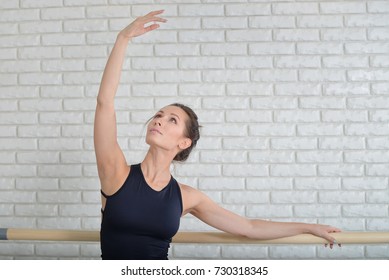Ballerina stretches herself near barre in the classroom, beautiful women weared in black bodysuit practicing ballet