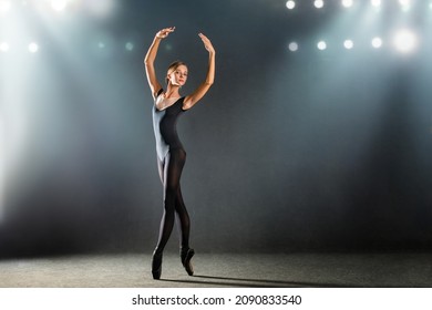 ballerina in a tight-fitting suit is dancing on a black background on pointe shoes, the silhouette is illuminated by sources of color.