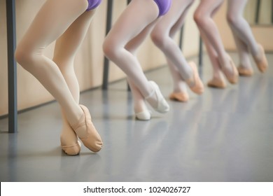 Ballerina training at hall, cropped image. Legs of young ballerinas having practice near ballet barre. Little dancers legs in pointe shoes doing exercises.