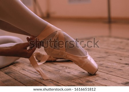 the ballerina tying the ribbons of pointes while sitting on the floor