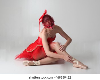 ballerina wearing a red mask and a red tutu and pointe shoes, sitting on the floor. - Powered by Shutterstock