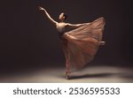 Ballerina. Young graceful woman ballet dancer, dressed in professional outfit, shoes and beige weightless skirt is demonstrating dancing skill. Beauty of classic ballet.