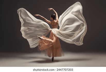 Ballerina. Young graceful woman ballet dancer, dressed in professional outfit, shoes and beige skirt with white flying fabric wings.Girl is demonstrating dancing skill. Beauty of classic ballet dance  - Powered by Shutterstock