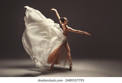 Ballerina. Young graceful woman ballet dancer, dressed in professional outfit, shoes and beige skirt with white flying fabric wings.Girl is demonstrating dancing skill. Beauty of classic ballet dance 