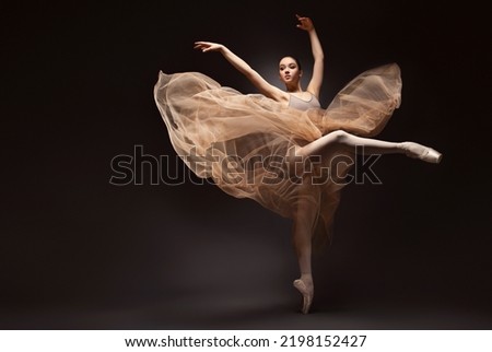 Ballerina. Young graceful woman ballet dancer, dressed in professional outfit, shoes and beige weightless skirt is demonstrating dancing skill. Beauty of classic ballet.